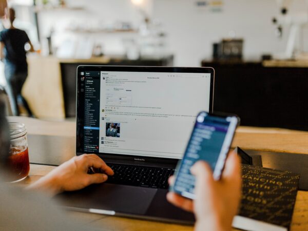 person typing on computer and holding phone