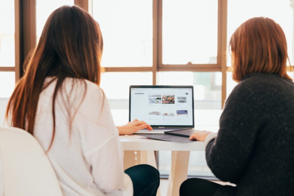 two women sitting in front of a computer screen