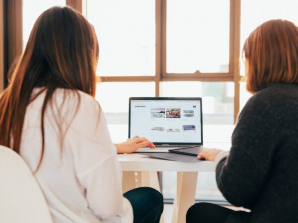 two women sitting in front of a computer screen